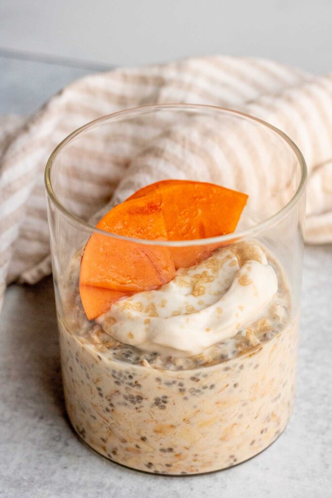 Sugar cookie oats in a jar topped with yogurt and persimmon slices and a pinch of brown sugar.