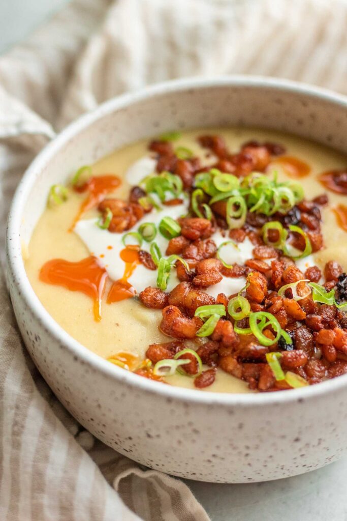 Large cozy bowl of vegan potato soup topped with crispy tempeh crumbles, scallions and vegan sour cream.