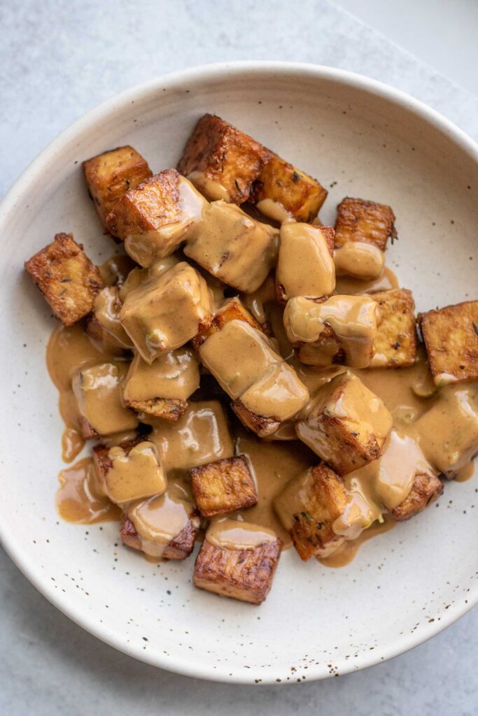Mixing the peanut sauce with the baked tofu in a bowl.