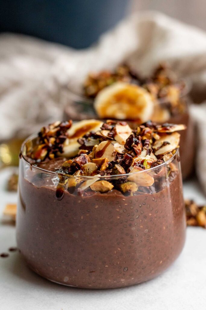 Close up of a jar of chocolate chia pudding from the side and topped with banana slices and nut granola.