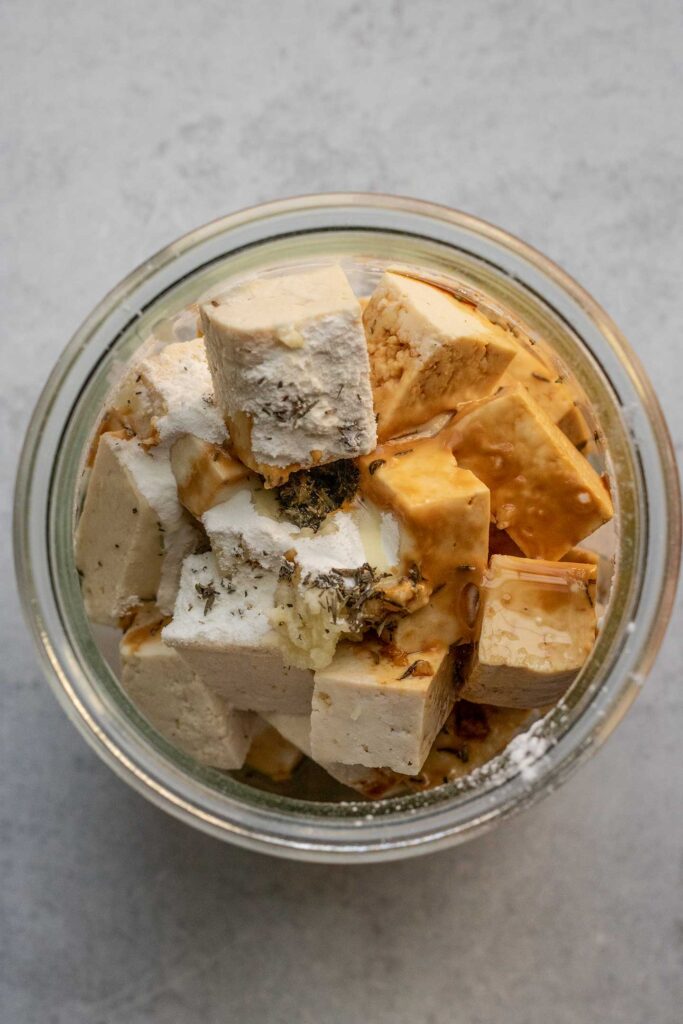Placing cubed tofu with seasonings and oil in a container.