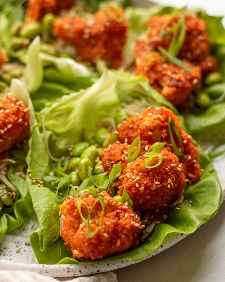Gochujang cauliflower placed in a lettuce wrap with edamame, noodles and topped with scallions and sesame seeds.