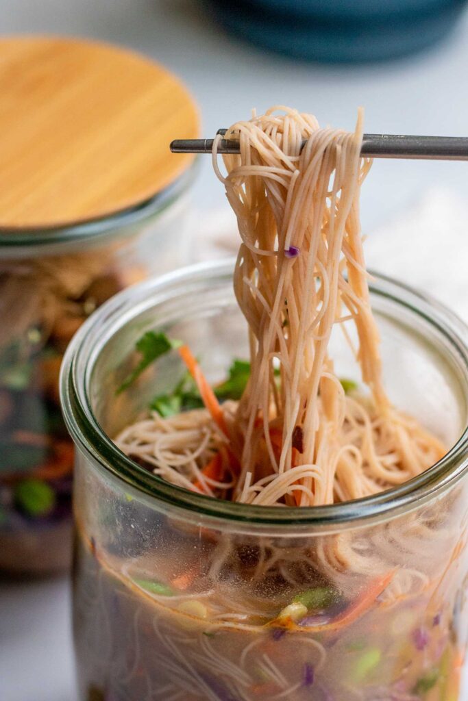 Pulling noodles from a jar of homemade instant noodles with chopsticks.