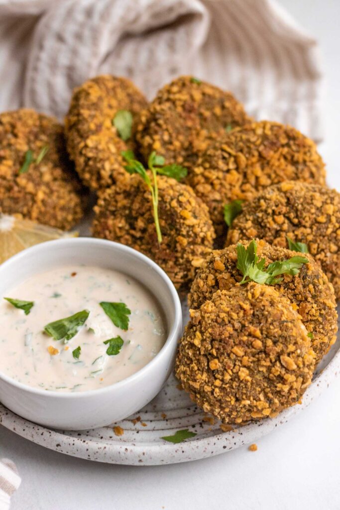 Side view of a plate of lentil patties being served with some yogurt dipping sauce in a bowl.