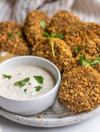 Close up view of a plate lined with lentil patties served with a small bowl of yogurt dip.