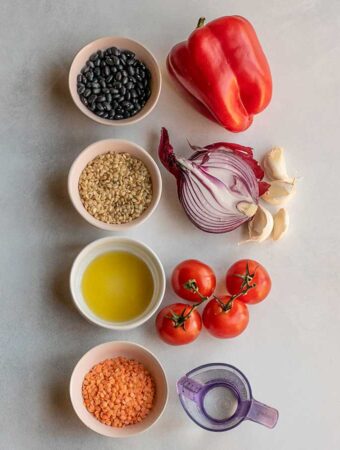 Pairing together black beans with bell pepper, rice with onions and garlic, oil with tomatoes, and red lentils with water using separate bowls on a working surface.