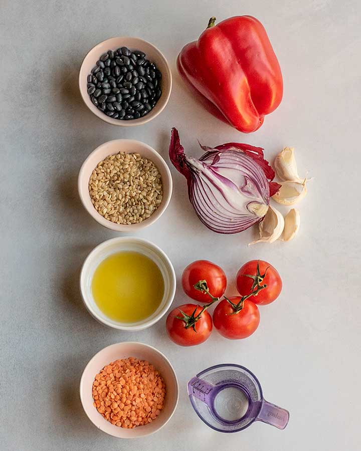 Pairing together black beans with bell pepper, rice with onions and garlic, oil with tomatoes, and red lentils with water using separate bowls on a working surface.