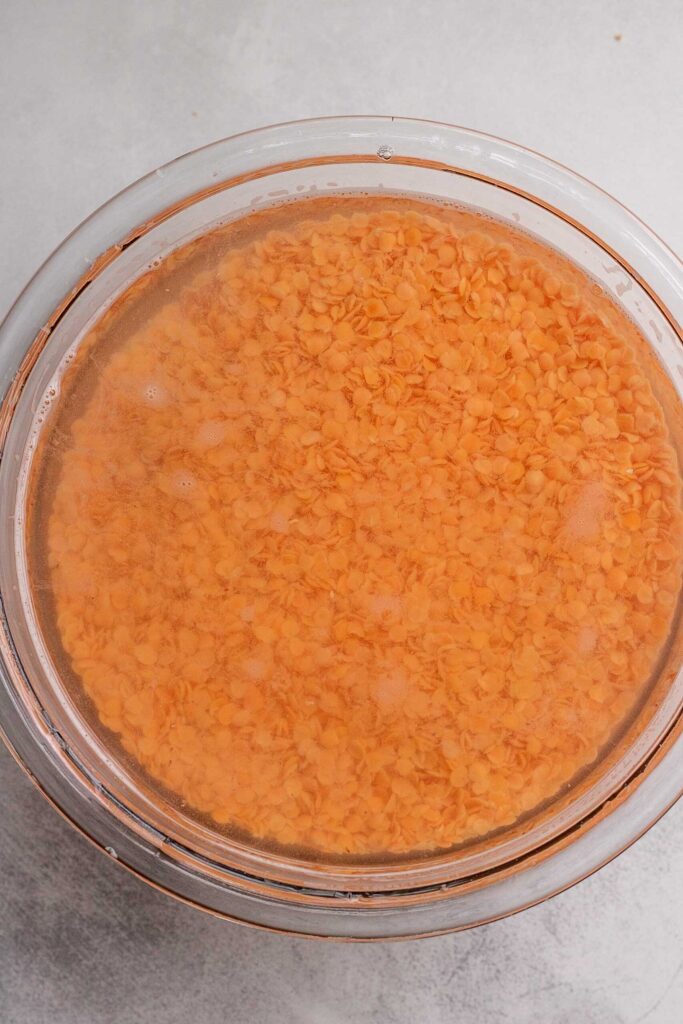 Bowl of red lentils being soaked in a bowl of water.