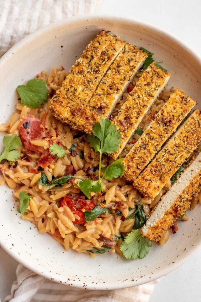 Top down view of a bowl of tomato orzo with crispy tofu on top.