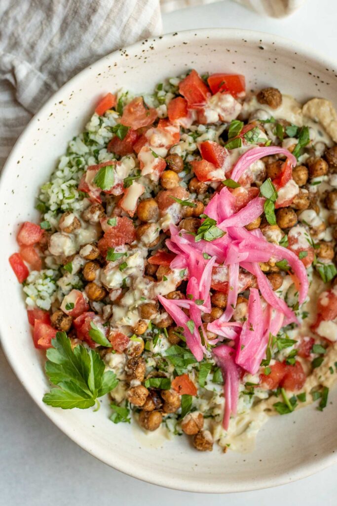Top down view of a large bowl with herby rice topped with chickpeas, tomatoes, and pickled onions.