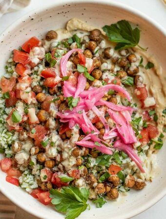Close up of a bowl of herby rice salad with chickpeas, tomatoes, pickled onions and hummus dressing.
