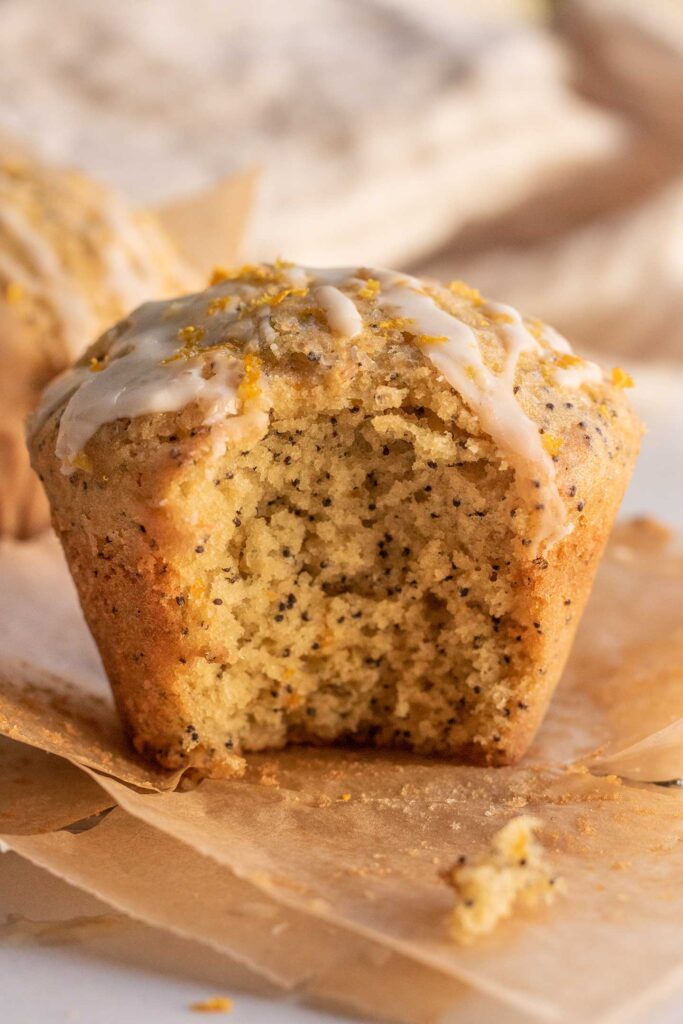 Close up view of a muffin that has been bitten showing the inside crumb over the parchment liner.