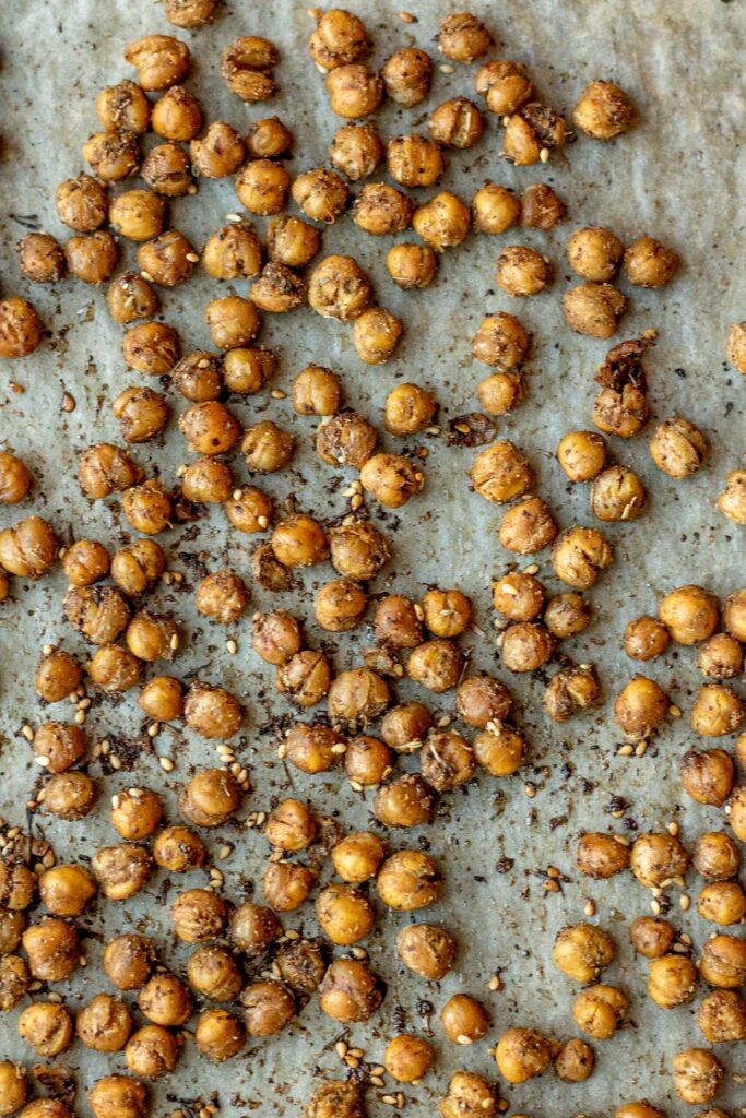 Fully roasted chickpeas on a parchment lined baking tray.