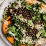 Plate of mashed sweet potato halves topped with roasted kale, lentils and a tahini sauce.