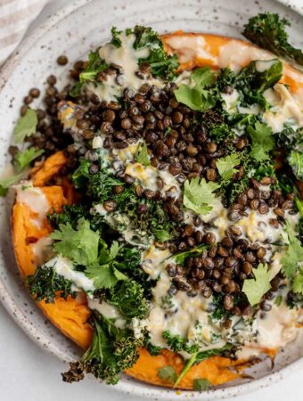 Plate of mashed sweet potato halves topped with roasted kale, lentils and a tahini sauce.