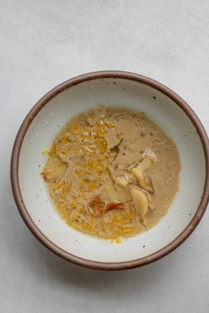 Tahini, lemon juice, mustard and roasted garlic in a small white mixing bowl.