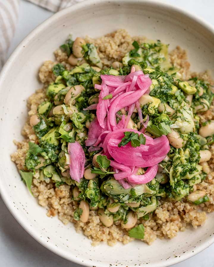 Close up of a bowl of quinoa topped with some herby white bean salad and pickled onions.