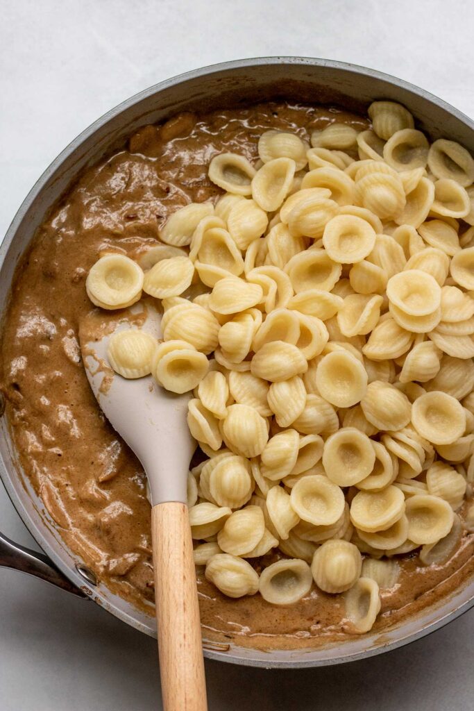 Stirring in orecchiette pasta into the caramelized onion sauce in a pan.