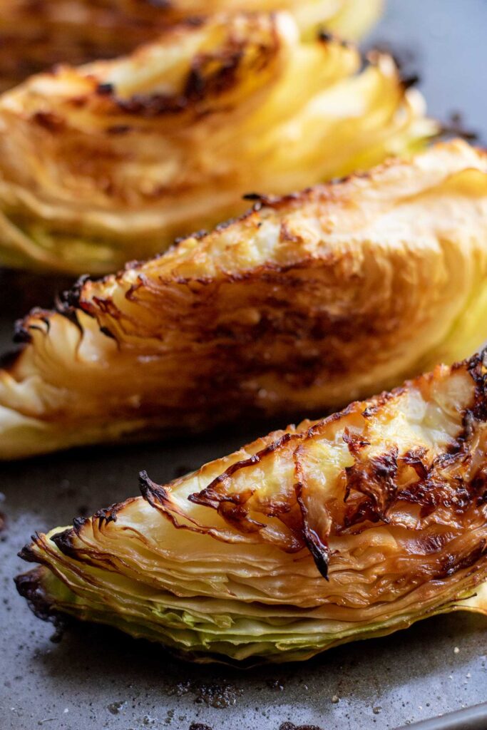 Roasted and charred cabbage wedges arranged cut side up on a baking tray in a row.