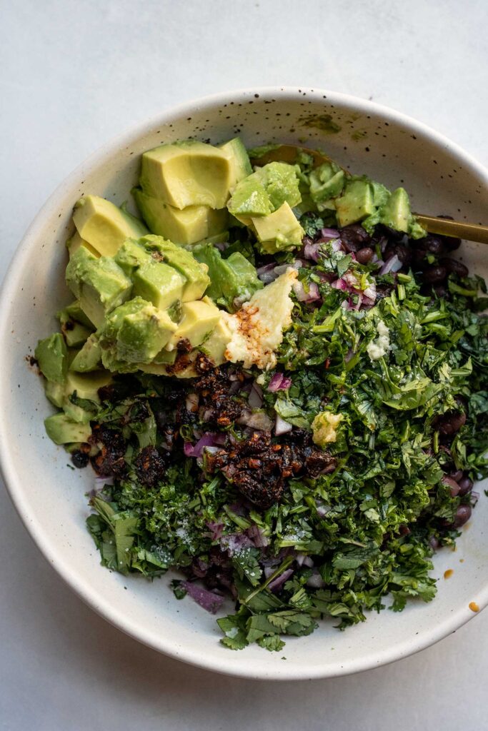 Mixing together the black beans, avocado, cilantro, garlic and ginger with the chili oil dressing in a large white bowl.