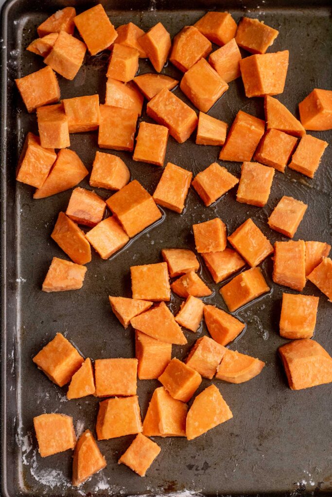 Cubed sweet potatoes coated in oil and cornstarch on a naked sheet pan.