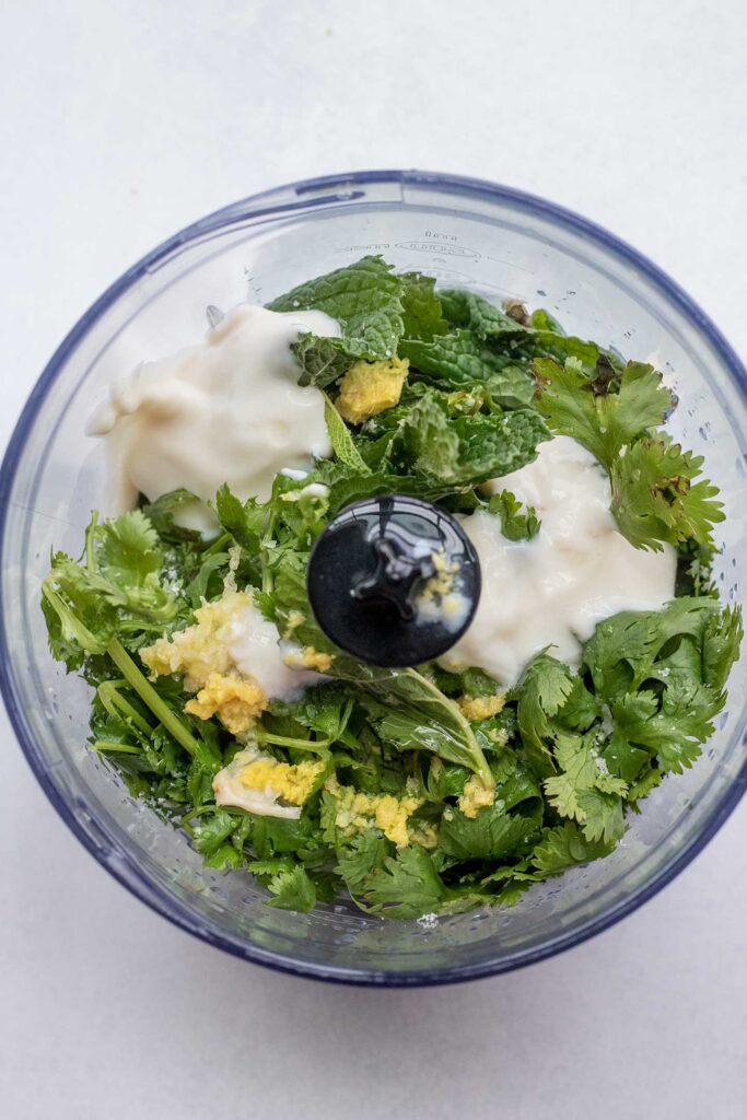 Mini food processor filled with mint, cilantro, garlic, ginger, and plant based yogurt.