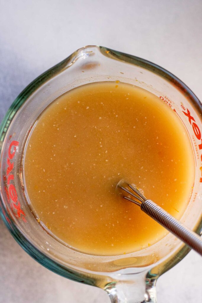 Large glass measuring cup filled with orange miso sauce ingredients being whisked together.
