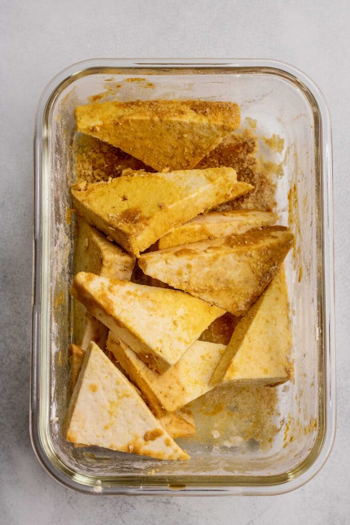 Tofu coated in nutritional yeast, cornstarch and soy sauce in a glass container.