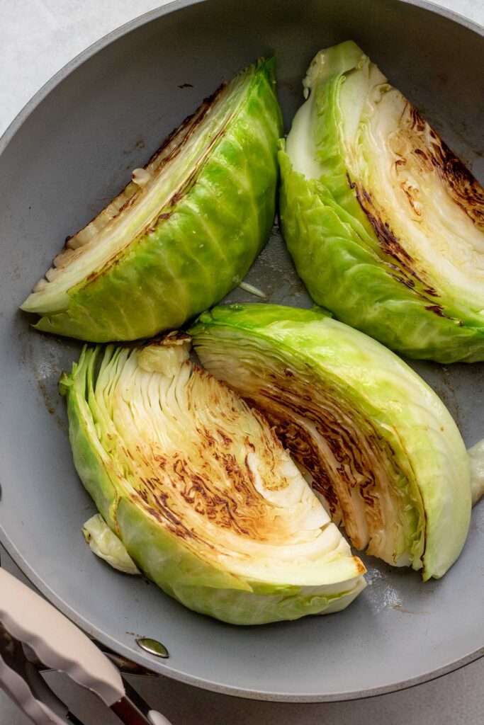 Searing cabbage wedges in a skillet.