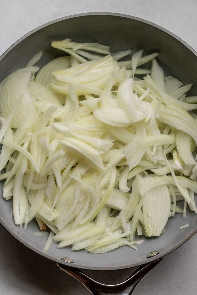 Cooking down onions in a large pan with a pinch of salt.