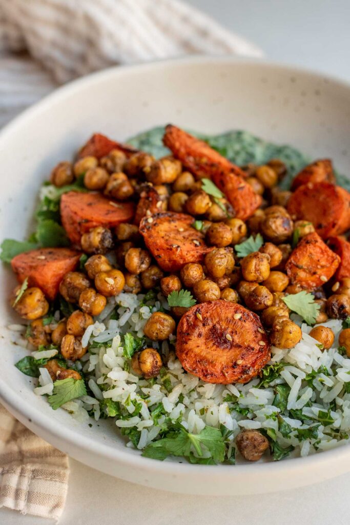 Side view of a bowl of roasted carrots and chickpeas over herby rice and yogurt sauce.