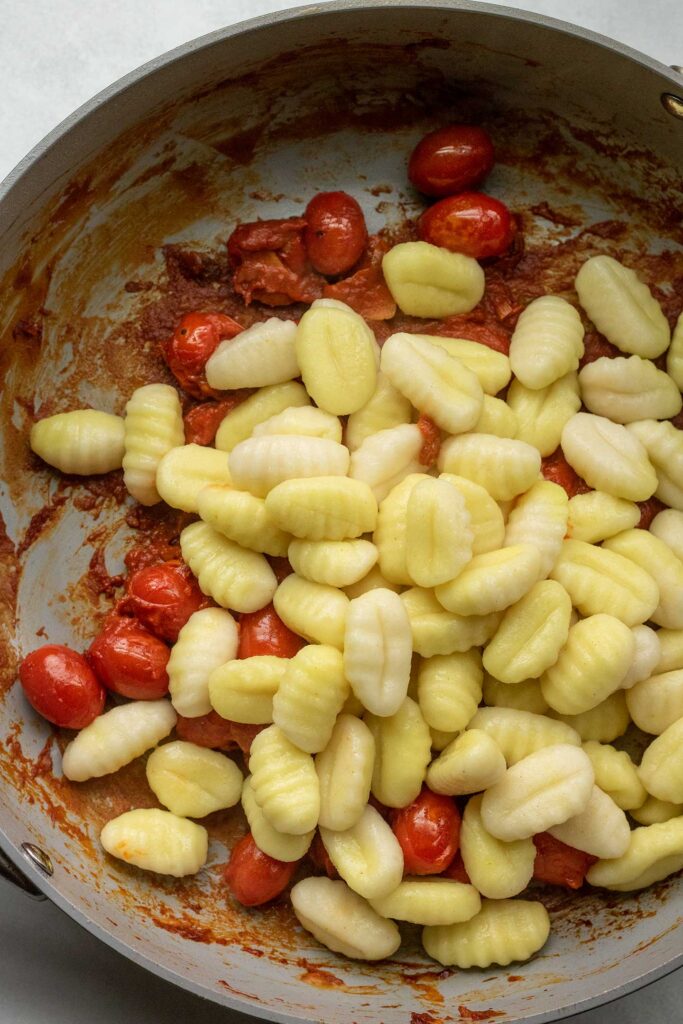 Adding the cooked gnocchi to the spiced tomato mixture.