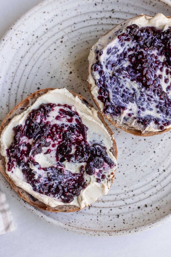 Blueberry bagels cut in half and spread with cream cheese and blueberry jam.