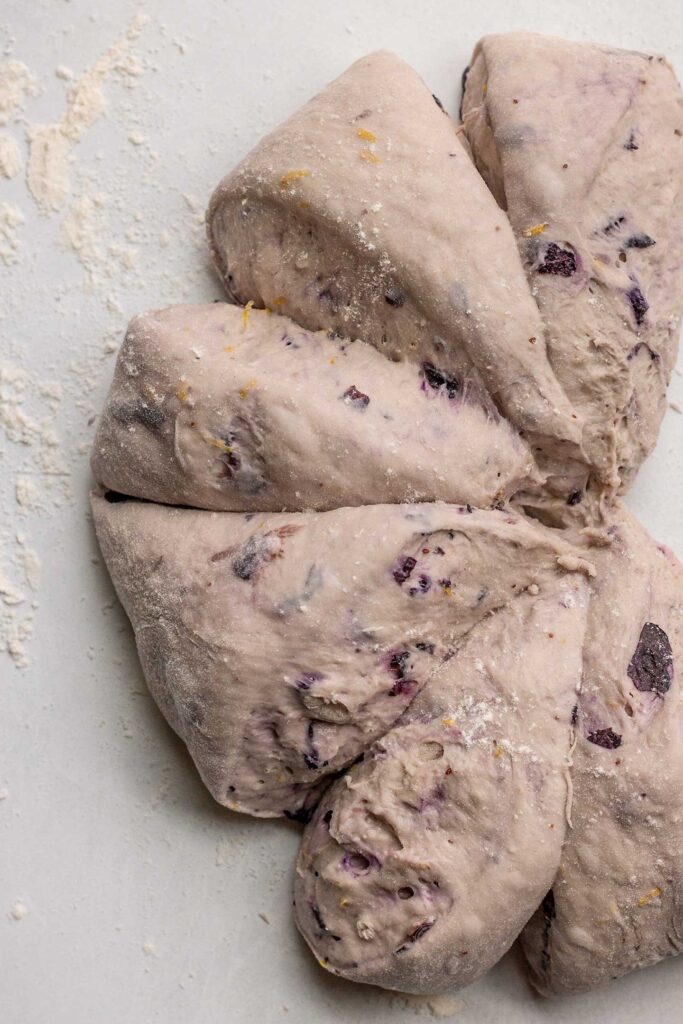 Blueberry dough sectioned into 8 pieces on a floured surface.