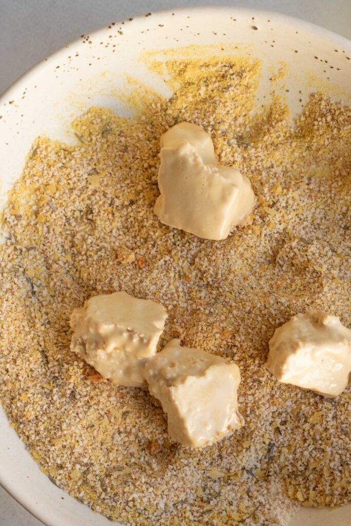 Breading the battered tofu in a bowl.