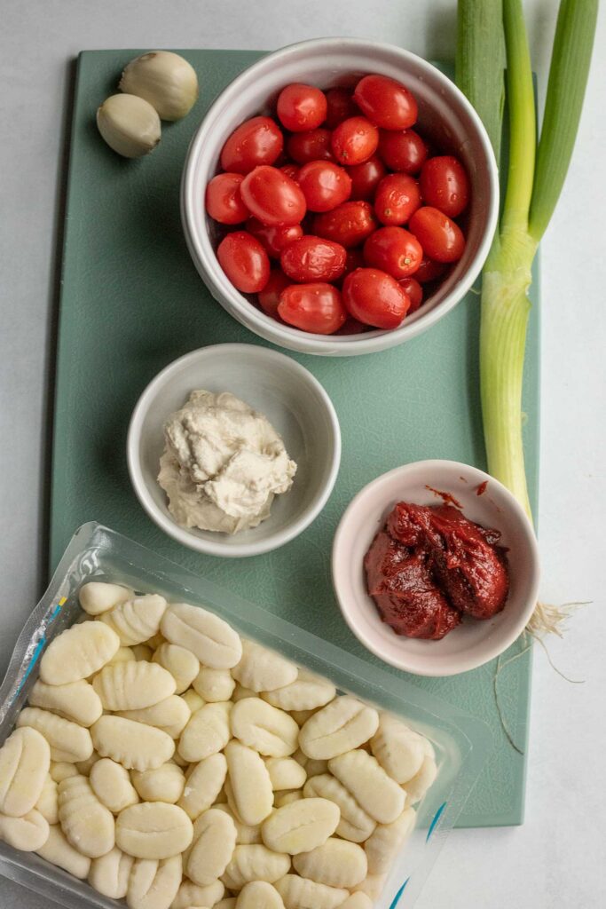 Gnocchi, gochujang, cherry tomatoes, scallion, cream cheese on a blue cutting board.