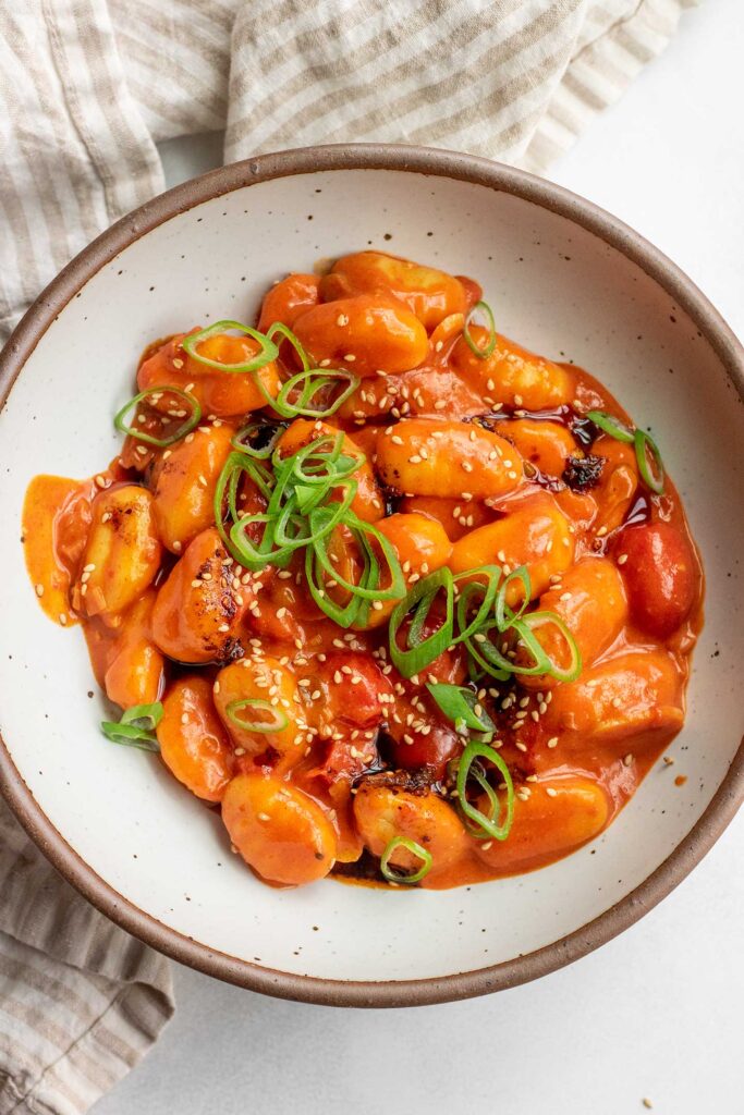 Bowl of tomato gochujang gnocchi topped with scallions and sesame seeds.