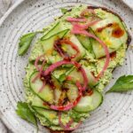 High protein edamame toast topped with cucumber slices, pickled onion, and chili oil and parsley.