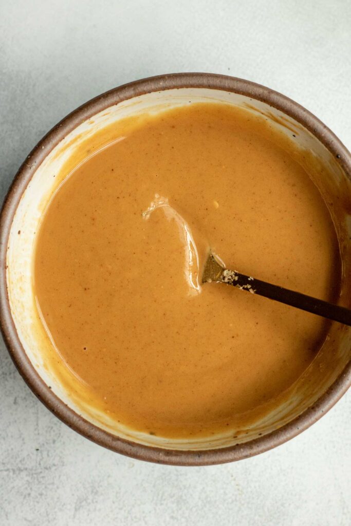 Stirring the hoisin peanut sauce together in a small bowl with a brown rim.