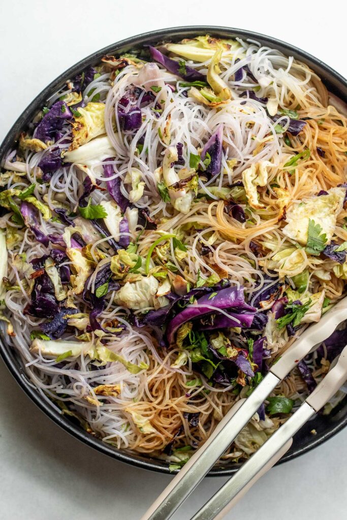 Mixing the noodles, cabbage and herbs together in a large bowl with tongs.