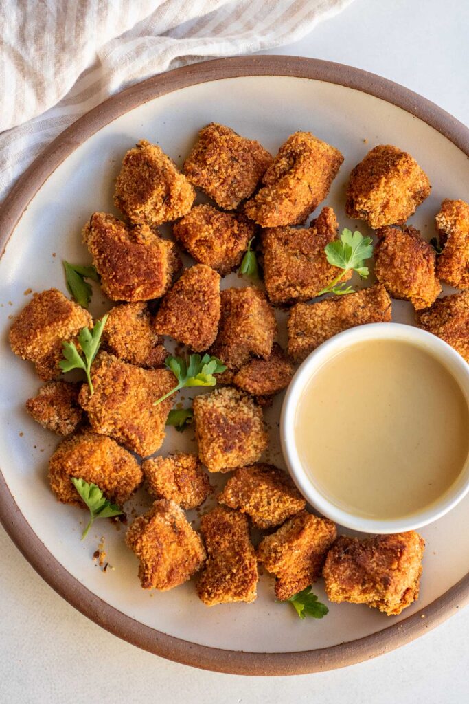 Plate of tofu nuggets and a vegan honey mustard dipping sauce in a bowl on the side.