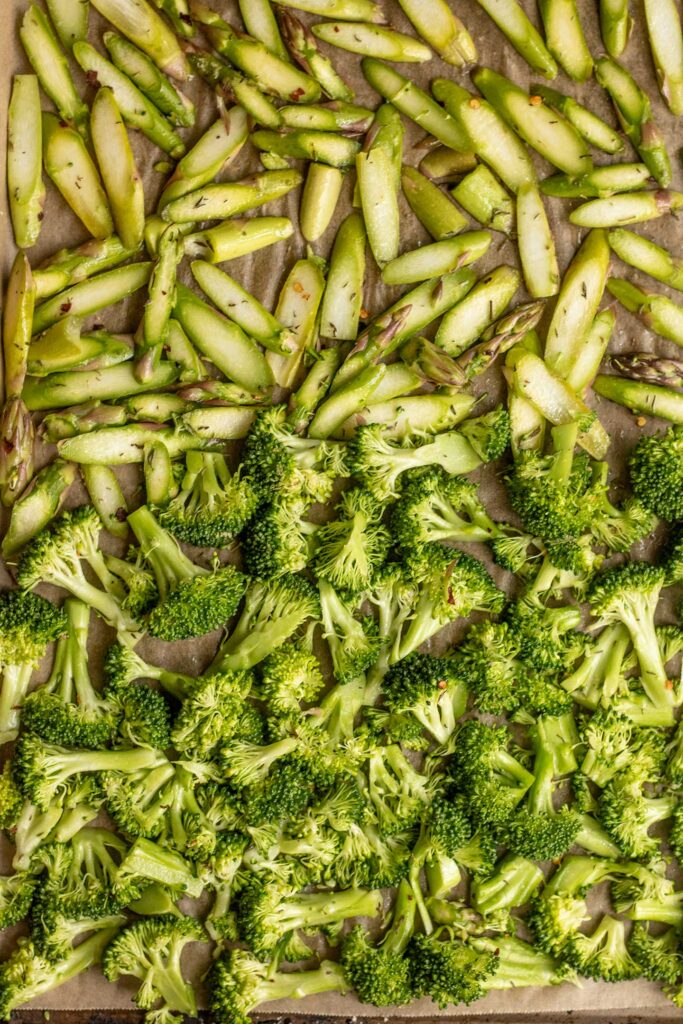 Seasoned broccoli and asparagus divided on a baking tray.