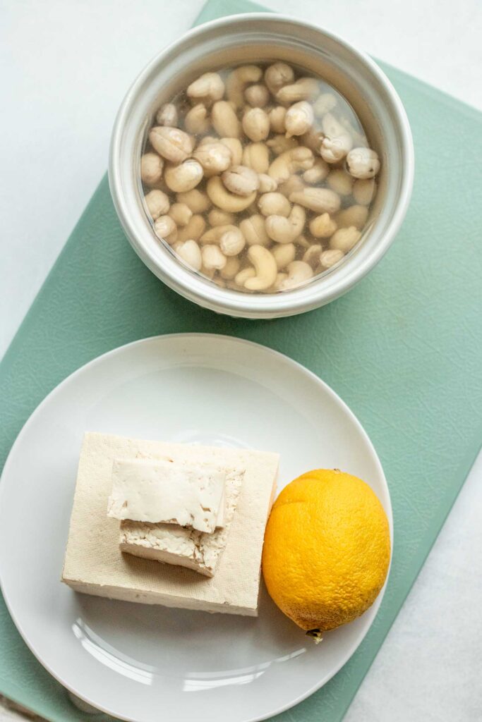 Soaked cashews, lemon and tofu on a cutting board.