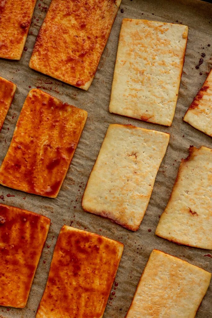 Flipping baked tofu to baste with more sauce on a baking tray.