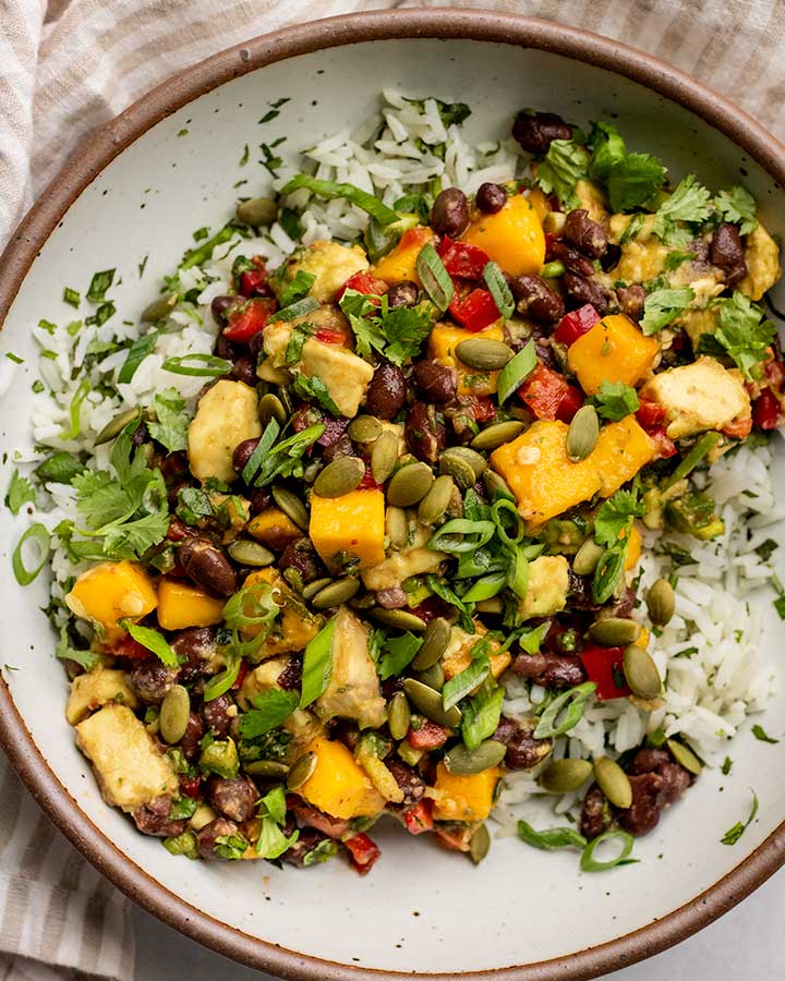 Serving bowl filled with coconut rice, black bean mango salsa and topped with pepitas.