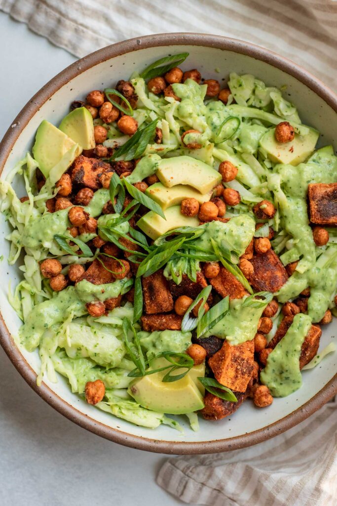 Bowl of cilantro lime slaw topped with roasted sweet potatoes, crispy chickpeas and sliced avocado.