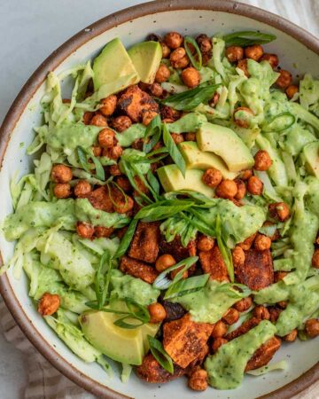 Close up view of a bowl of slaw topped with crispy chickpeas, sweet potatoes and sliced avocado.