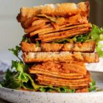 Gochujang tofu sandwich cut in half and stacked on a plate to show a stuffed filling of tofu slices, lettuce, pickled cucumber, carrots and kimchi.