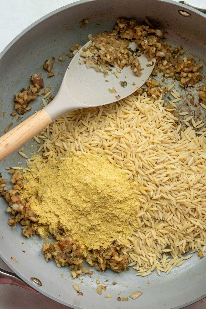 Stirring in the nutritional yeast and orzo into the skillet to toast up.