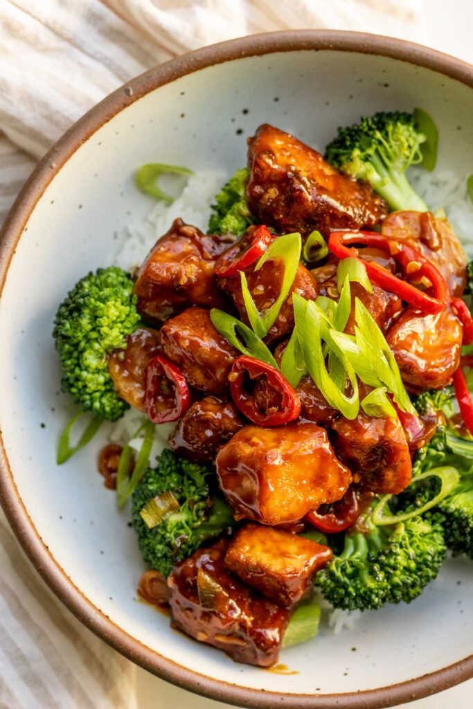 Bowl of rice topped with steamed broccoli, saucy tofu and scallions.